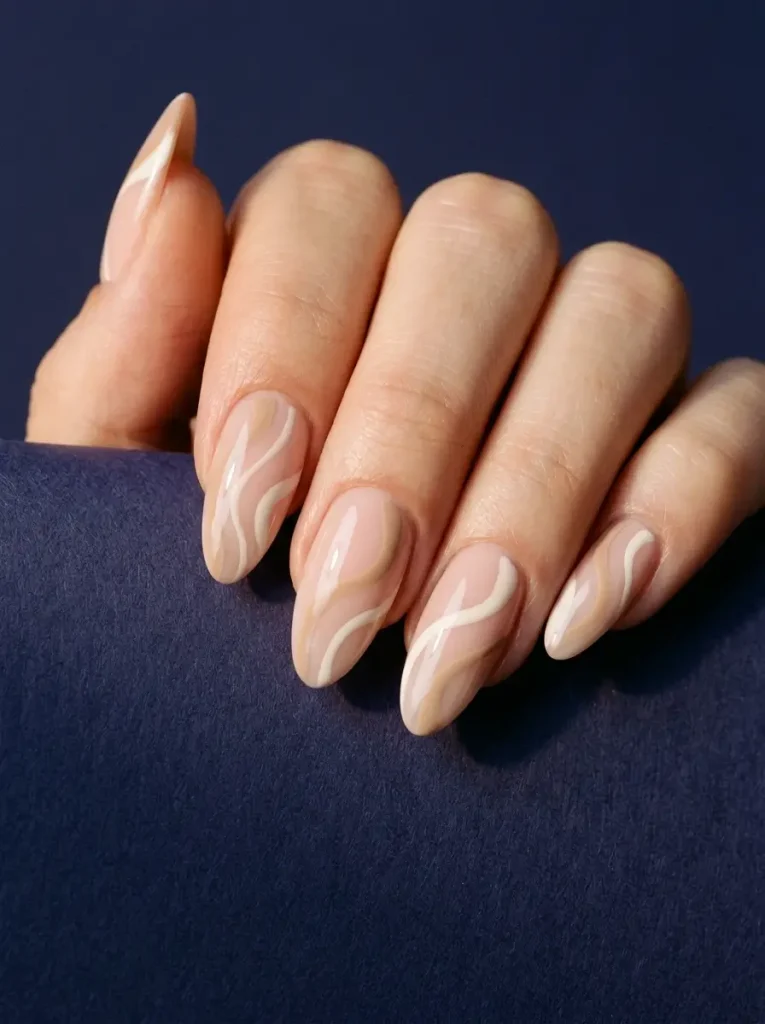 Long almond nude nails with soft beige and white abstract swirls, glossy finish, on light skin