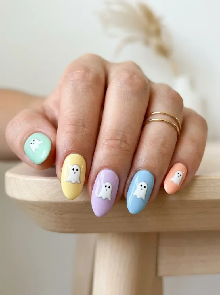 Short almond nails in five different pastels, each with a small white ghost with a fine gray outline, on a light skin tone