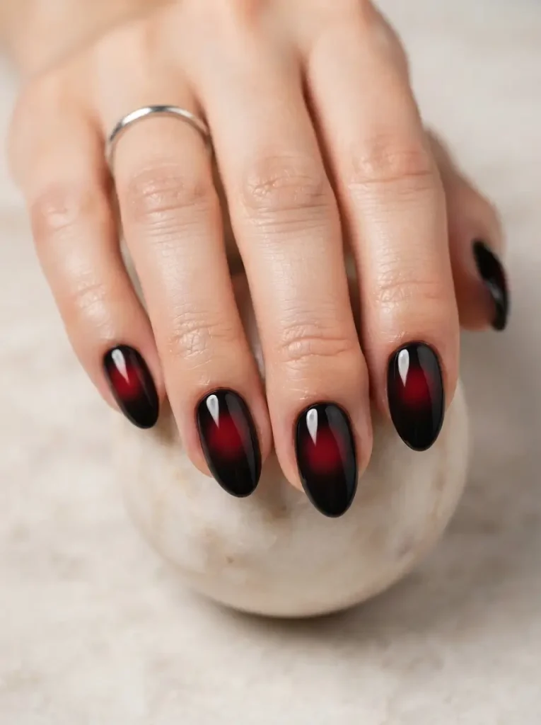 Almond vampire nails with a soft round red glow in the center of each nail fading to black edges, on a fair skin tone