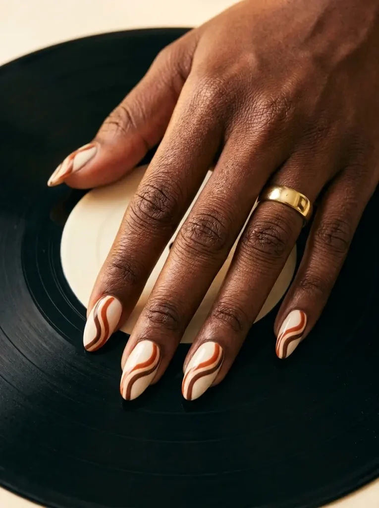 28 Fall Nail Designs for 2026, From Simple to Classy 10 Medium almond nails with clean 70s-style wave bands in rust, cream and chocolate on every nail, on a deep skin tone