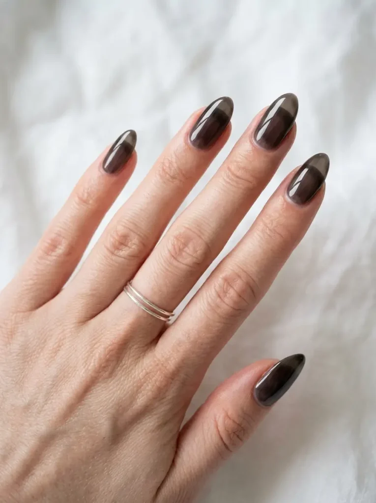Medium almond nails in sheer smoky black jelly polish like smoked glass, on a fair skin tone