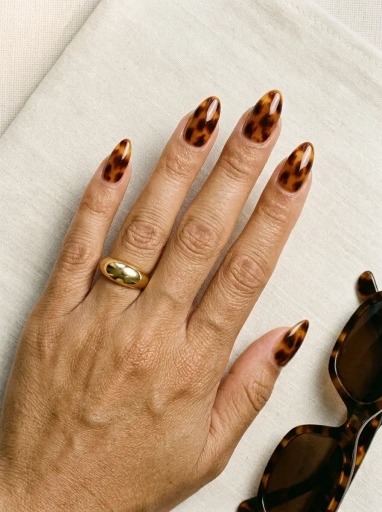 Medium almond nails in translucent caramel amber tortoiseshell with espresso blotches, on a medium skin tone