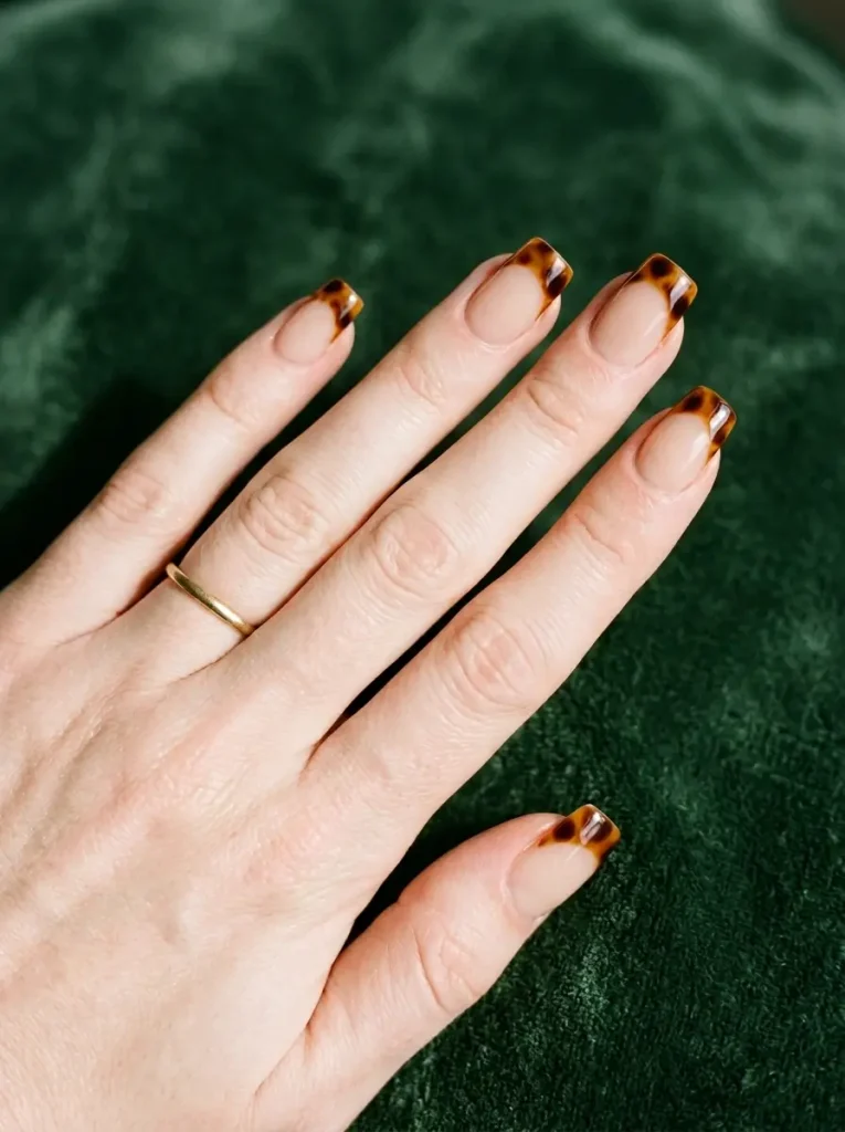 Medium squoval nails with a sheer nude base and tortoiseshell French tips, on a fair skin tone