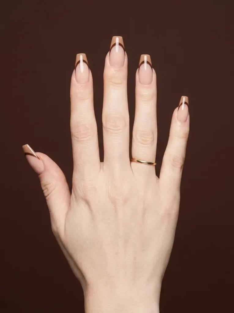 Long coffin nails with a double French tip in latte and espresso brown bands on a nude base, on a fair skin tone