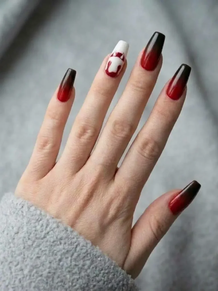 Coffin nails in a glossy red to black ombré with one white accent nail showing small fangs and a red drip, on a fair skin tone