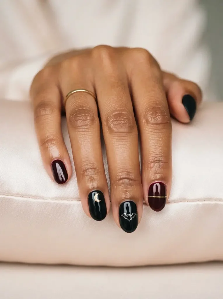 Short almond vampire nails with a different design on each nail, from a gold crescent to a silver bat outline, on a tan skin tone